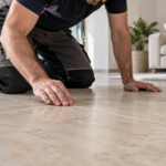 Tecnico inginocchiato osserva le fughe di un pavimento in gres beige in un soggiorno luminoso